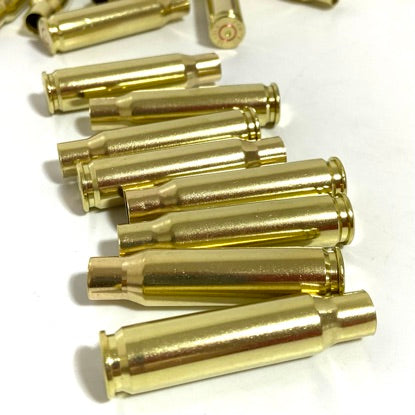 Ten gold 308 WIN brass cases neatly stacked horizontally in staggered rows on a clean white surface.