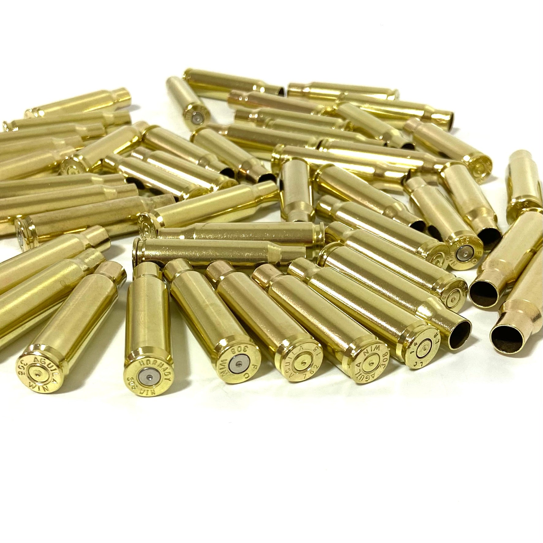Bulk lot of 308 WIN brass casings standing in front of a bulk mound on a white background showing base headstamps