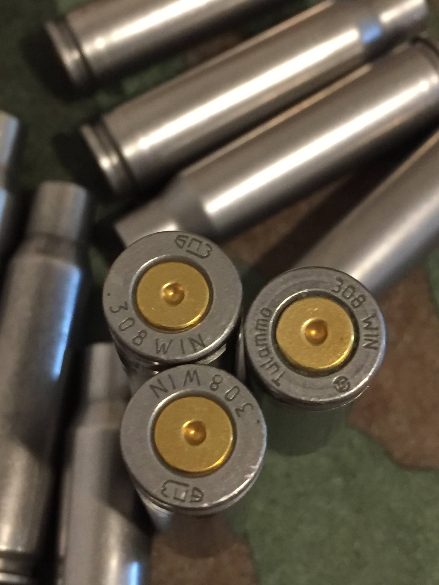 3 gray steel casings viewed from the base showing gold primers with 308 WIN headstamp text