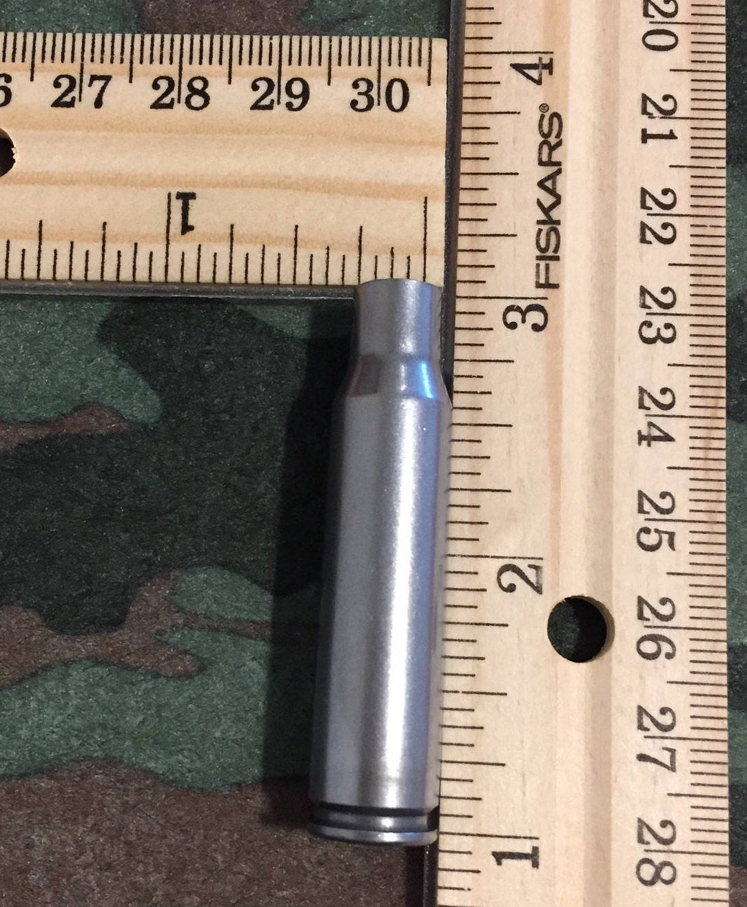 Single silver steel 308 Winchester rifle casing measured against a ruler, showing an overall length of about 2 inches