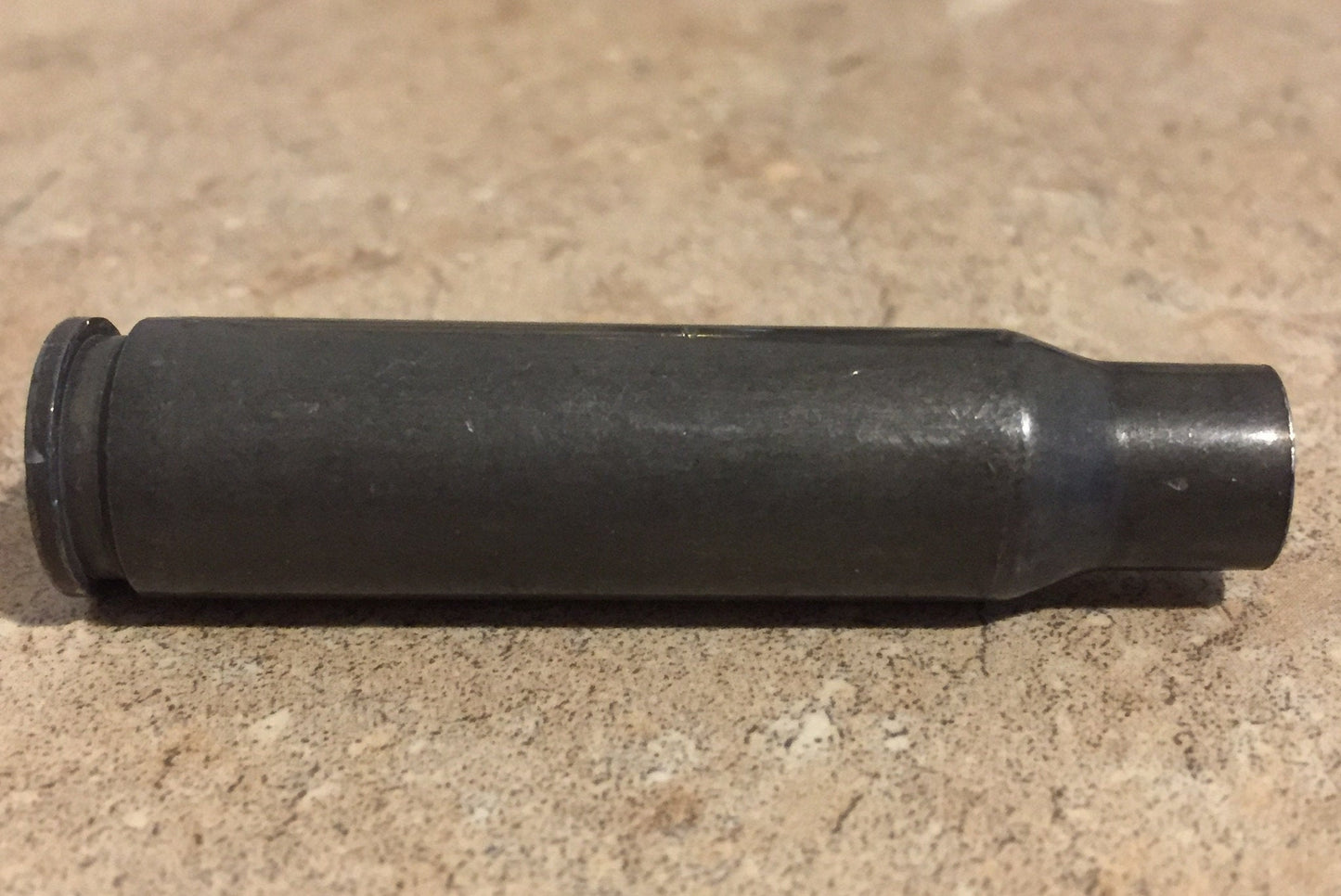 Single dark gray steel 308 Winchester rifle casing lying on a stone countertop, showing a bottlenecked shoulder