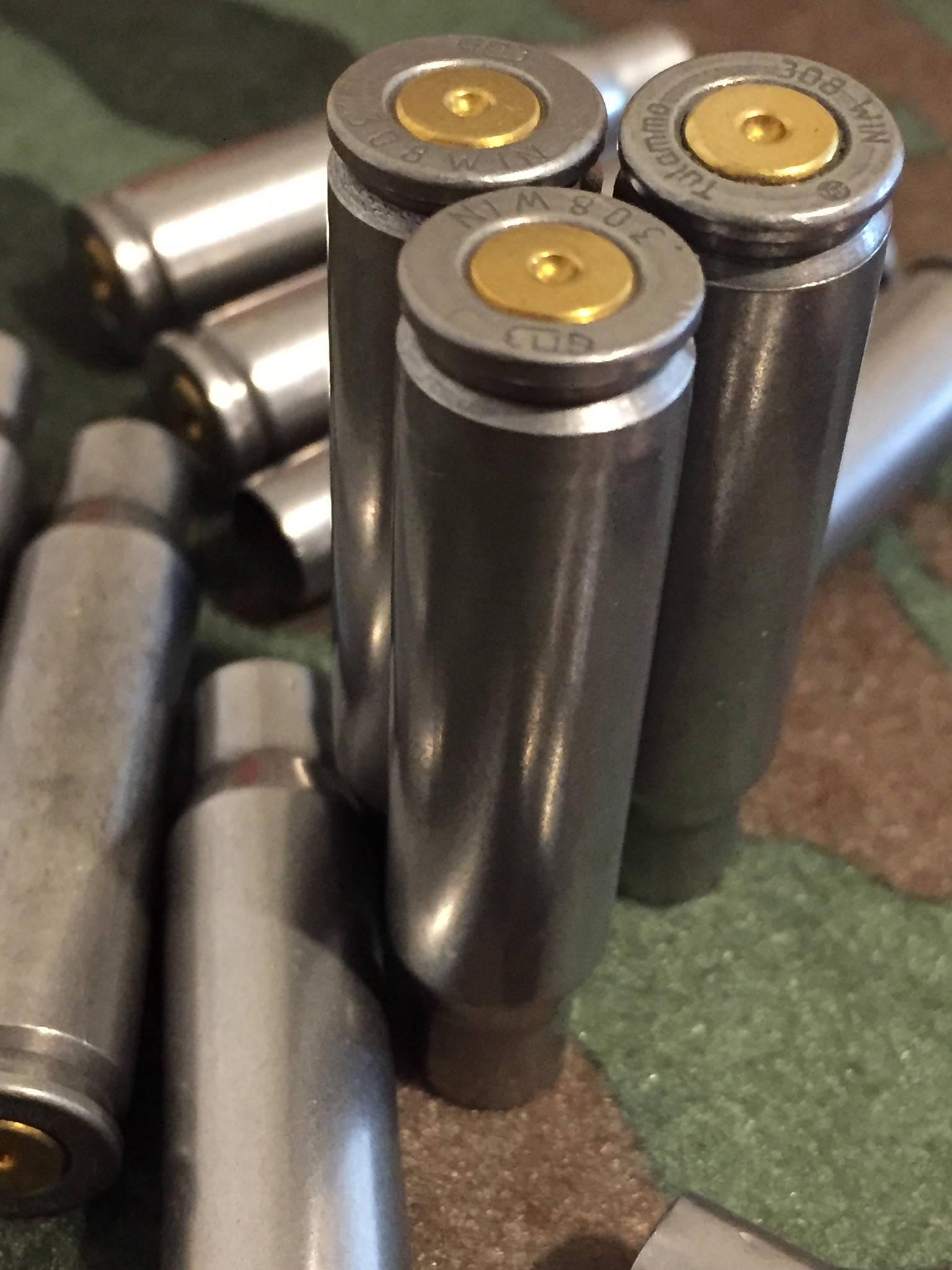 Three silver steel 308 Winchester rifle casings standing upright, showing gold headstamps stamped ‘308 WIN’ and ‘GDI’