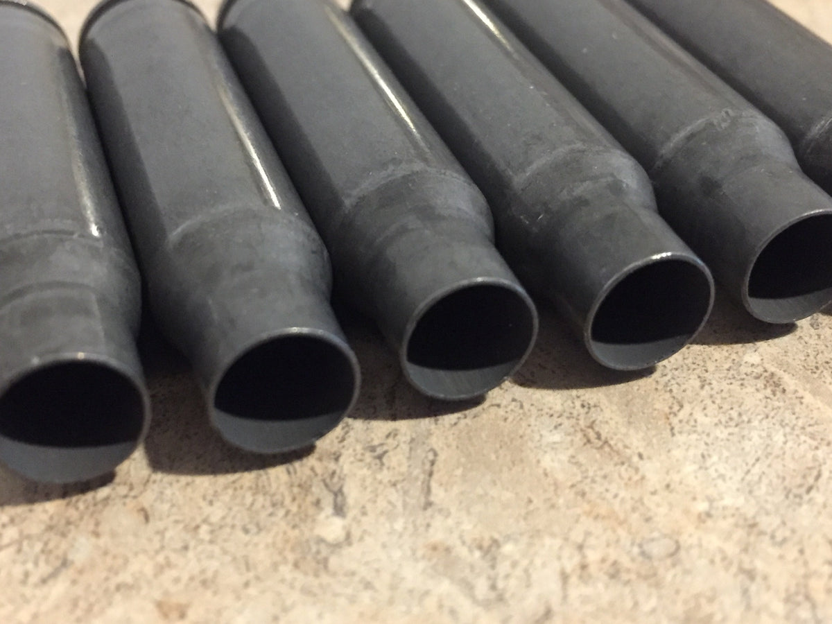 6 gray steel 308 casings lying in a row showing open mouths on a stone surface
