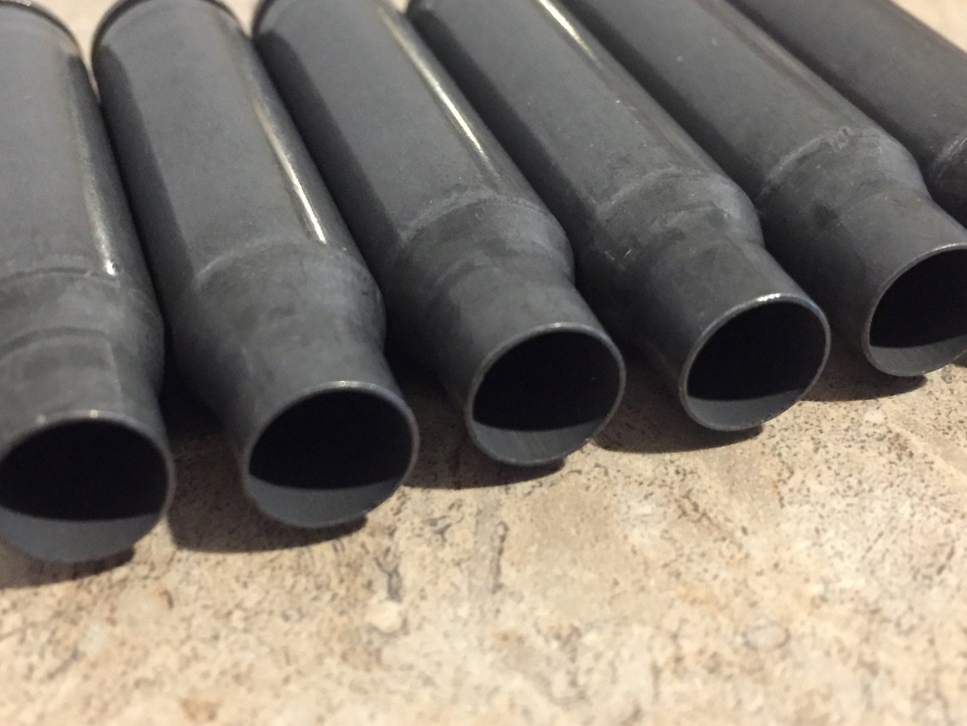 6 gray steel 308 casings lying in a row showing open mouths on a stone surface