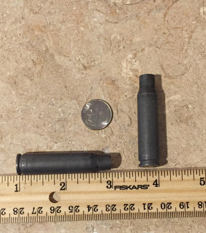 9 gray steel casings with drilled primers clustered together on a stone surface