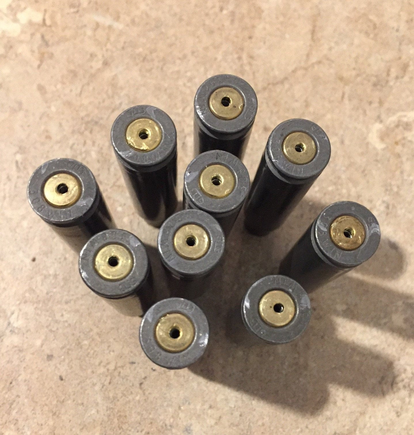 9 gray steel 308 casings viewed from the base showing small drilled holes in the primers