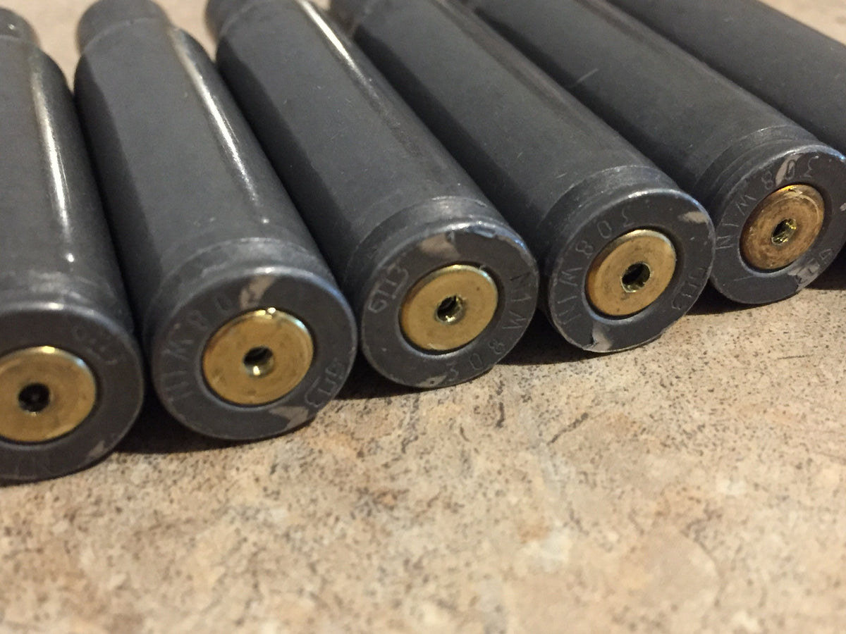 4 gray steel casings viewed close-up showing drilled primers with 308 WIN headstamp text