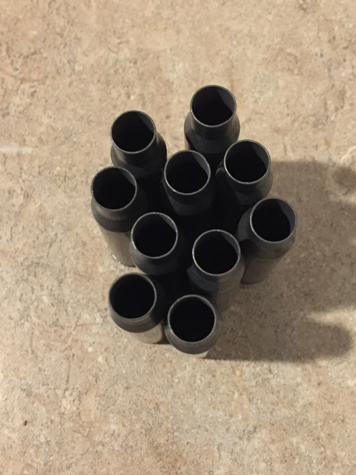 9 gray steel 308 casings with drilled primers clustered together on a stone surface