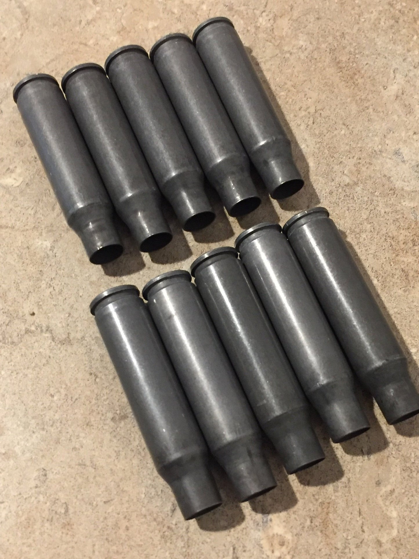 9 gray steel 308 casings viewed from above showing drilled open mouths on a stone surface