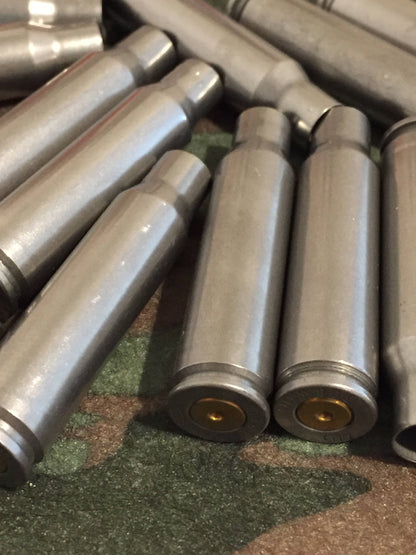 Silver steel 308 Winchester rifle casings lying on a camouflage background, showing gold primers on two upright bases