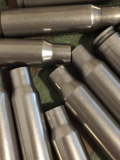 8 gray steel 308 casings lying together at angles on a stone surface