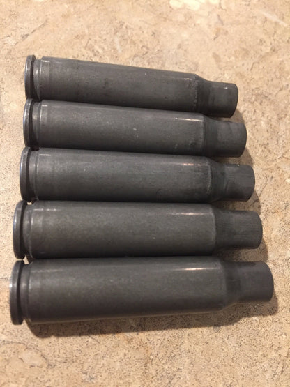 Five dark gray steel 308 Winchester rifle casings arranged in a row on a stone countertop
