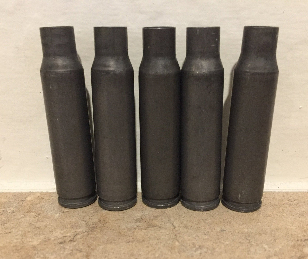 5 gray steel 308 casings standing upright against a white wall