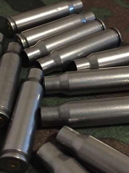 Pile of silver steel 308 Winchester rifle casings lying at angles on a camouflage background