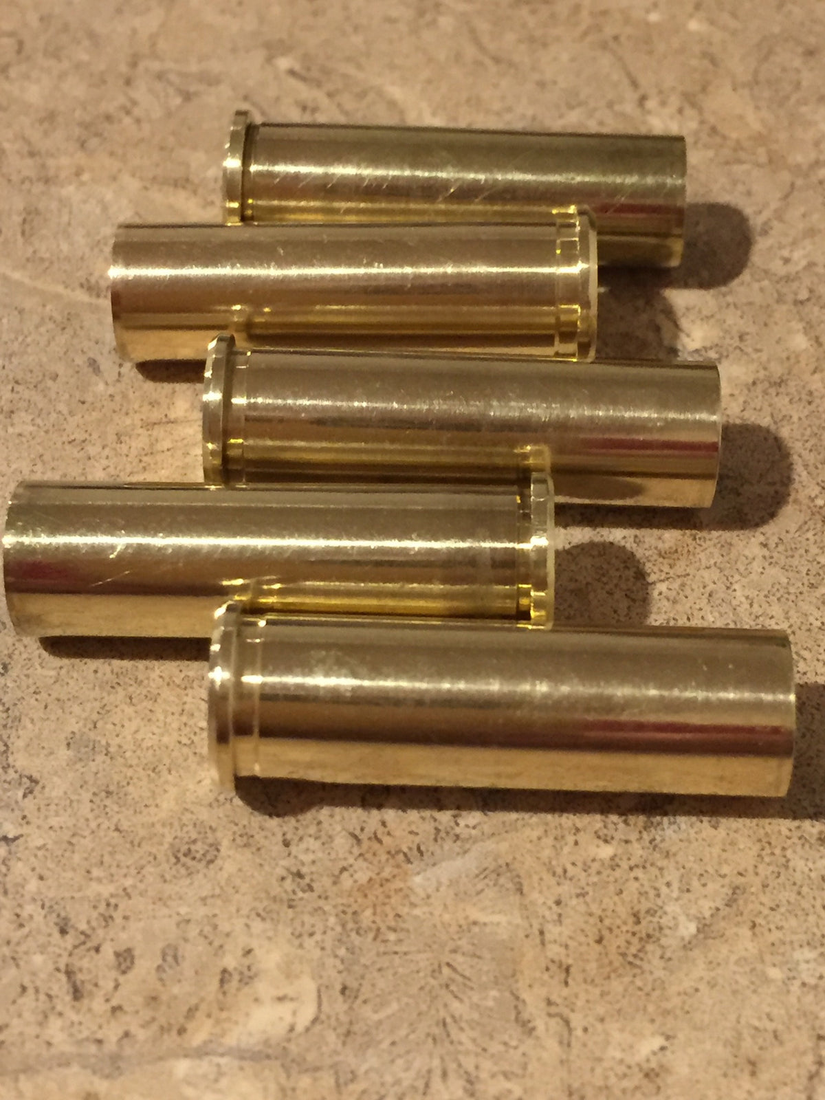 Five polished 357 Magnum brass cartridge cases arranged in a horizontal staggered stack on a tan stone surface.