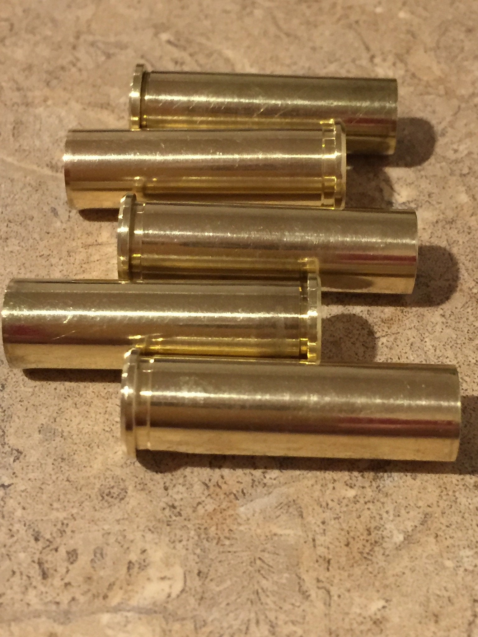 Five polished 357 Magnum brass cartridge cases arranged in a horizontal staggered stack on a tan stone surface.