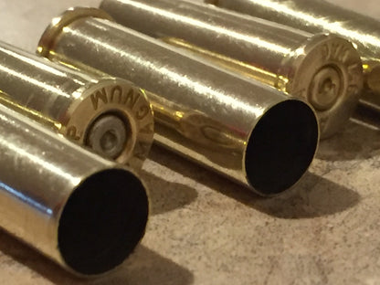 Macro view of four 357 Magnum brass casings lying horizontally, highlighting a stamped base rim and open mouths.