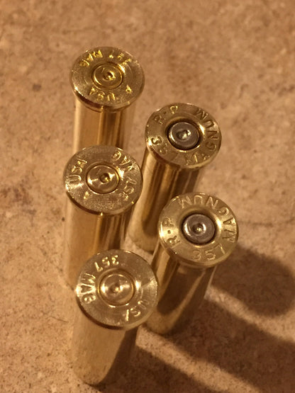 Five standing 357 Magnum brass casings viewed from above, showing base rims with mixed headstamps and spent primers.