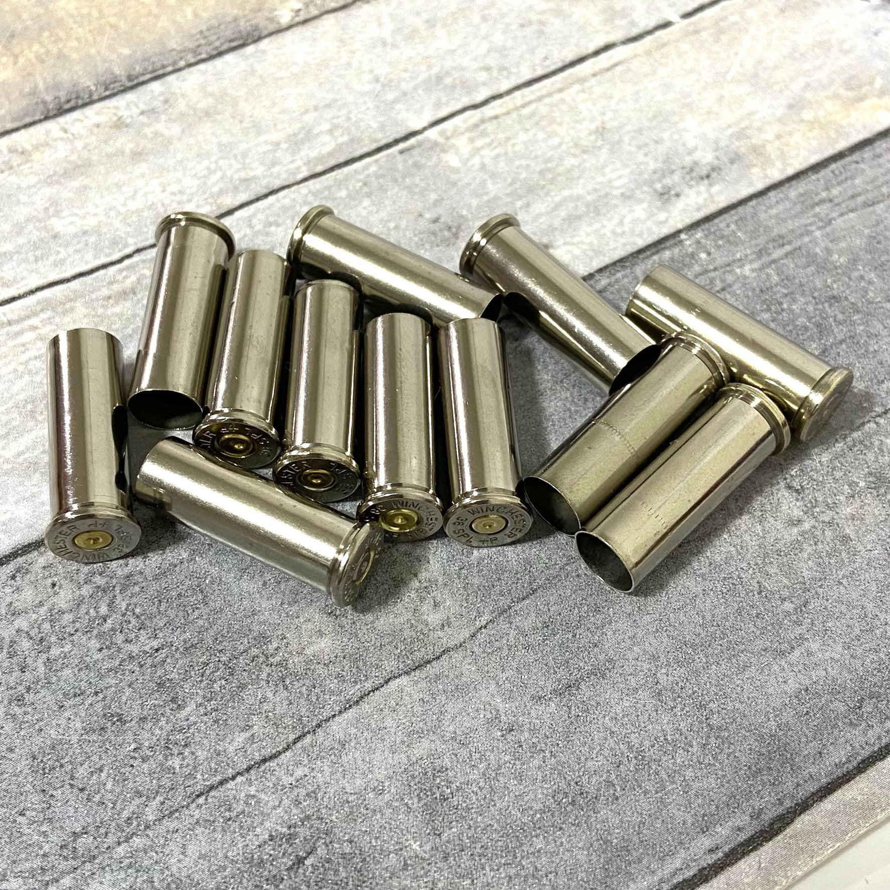 A scattered pile of spent silver nickel casings lying crossed on a weathered wood-plank surface.