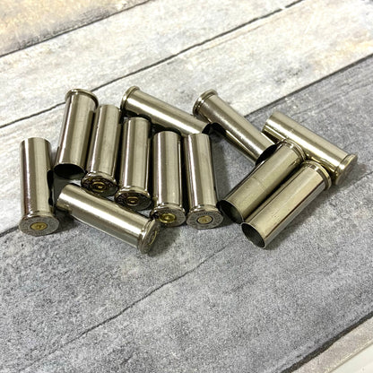 A scattered pile of spent silver nickel casings lying crossed on a weathered wood-plank surface.