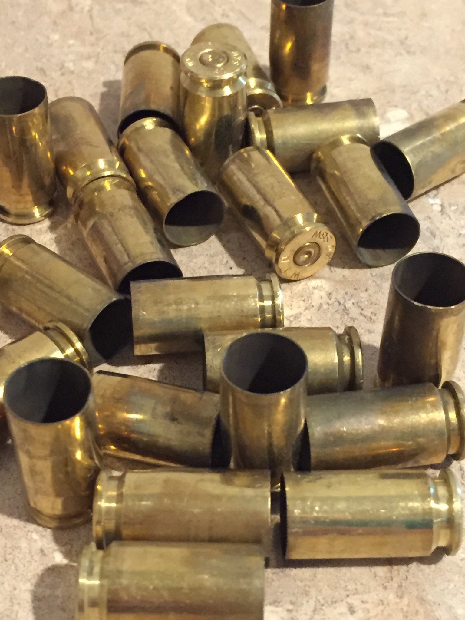 Pile of brass shells showing open ends and headstamps on solid surface