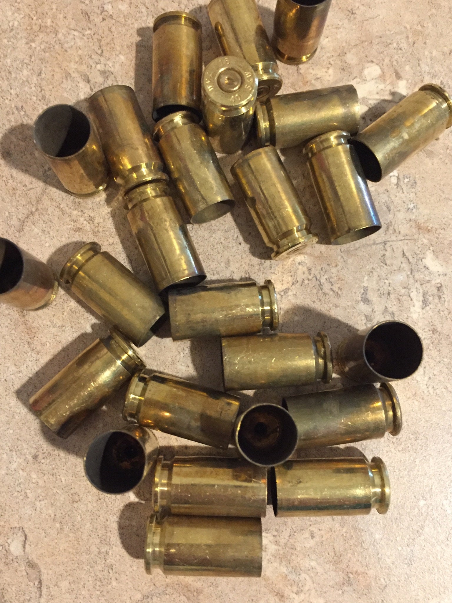 Pile of gold .40 S&W brass casings lying at angles on a stone surface, showing open mouths and headstamps
