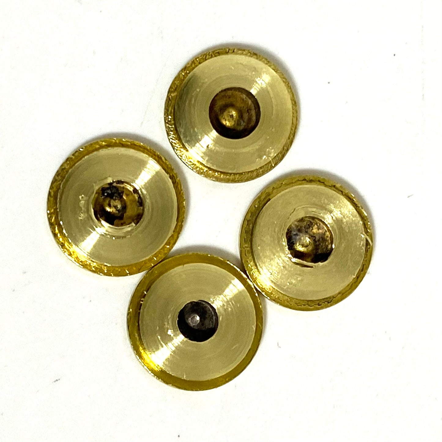 Four gold ammo slices arranged in a cluster, showing the concave interior side with tarnished centers.