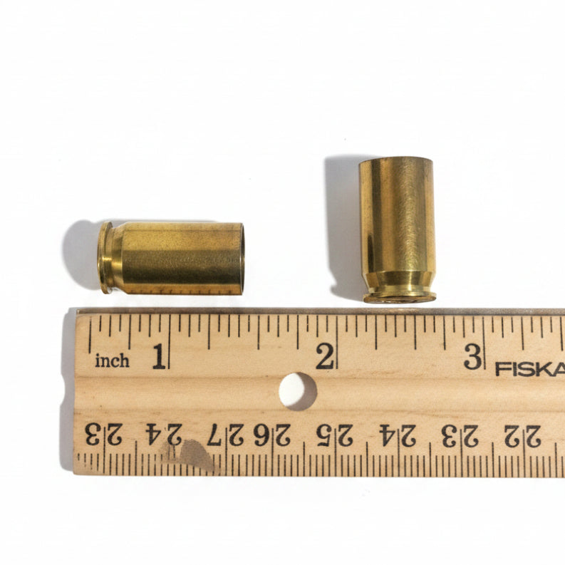 Two brass .45 ACP casings lying on a wooden ruler, each measuring approximately 0.9 inch in length from base to mouth