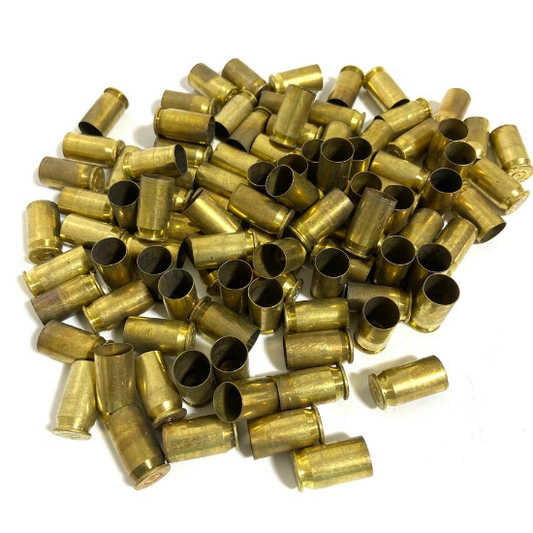 Large bulk pile of yellow-brass .45 ACP casings scattered loosely on white background, mixed open and closed ends, showing natural tarnish and firing wear