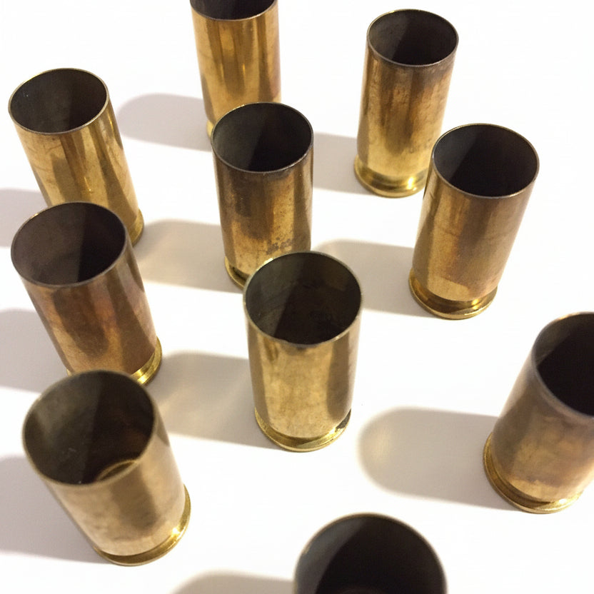 About 10 brass .45 ACP casings scattered at angles on white background, open mouths facing up, showing dramatic shadow and natural tarnish