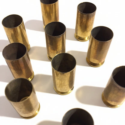 About 10 brass .45 ACP casings scattered at angles on white background, open mouths facing up, showing dramatic shadow and natural tarnish