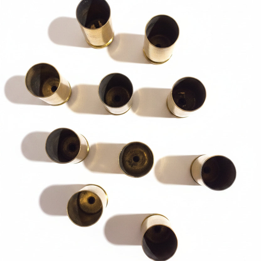 10 brass .45 ACP casings viewed from an angle showing their primer ends and bases, scattered on white background
