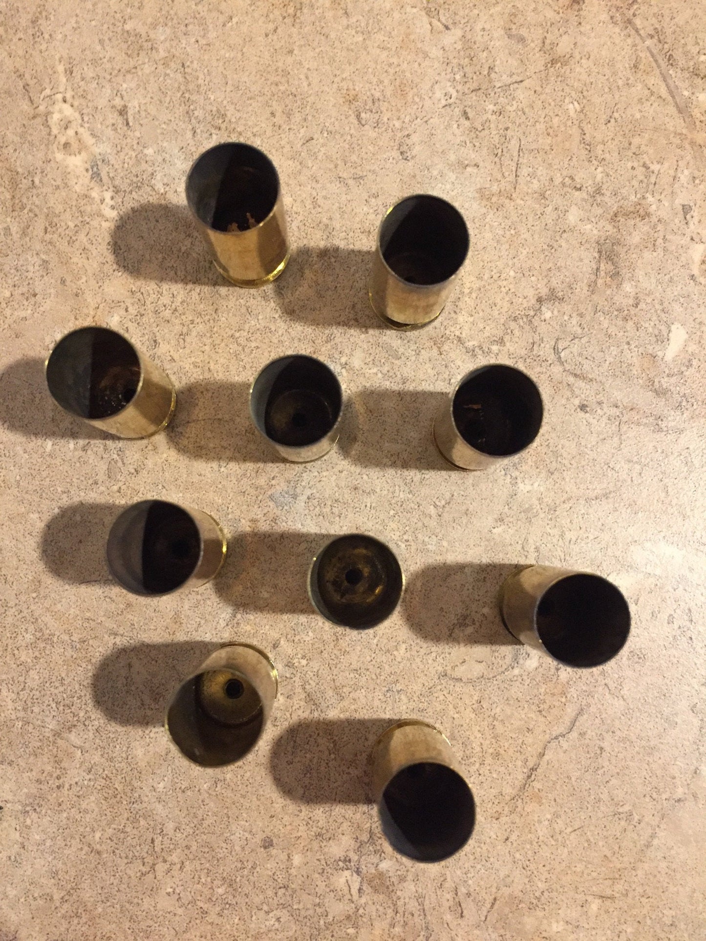Top-down view of ten uncleaned brass shell casings arranged on a speckled surface.
