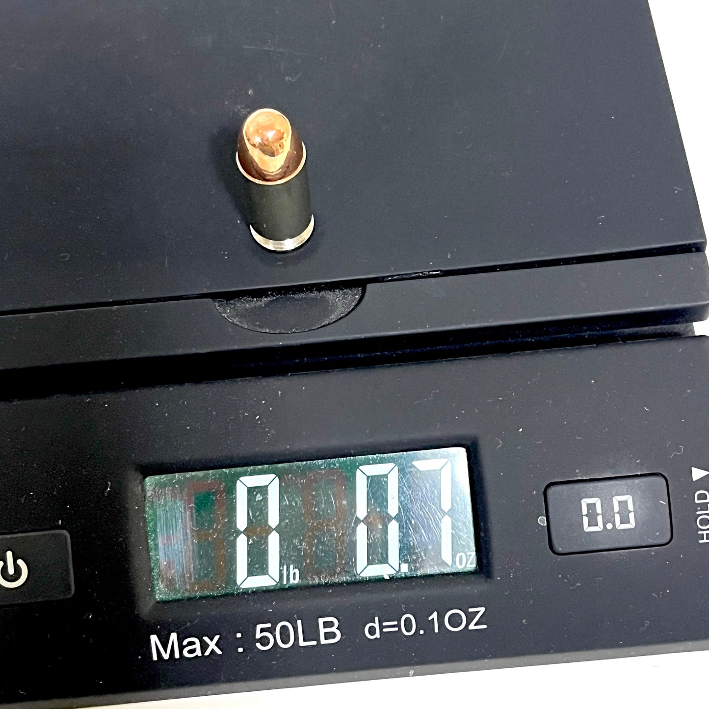 A single nickel 45 ACP dummy round placed on a digital scale, displaying a weight of 0.7 ounces.
