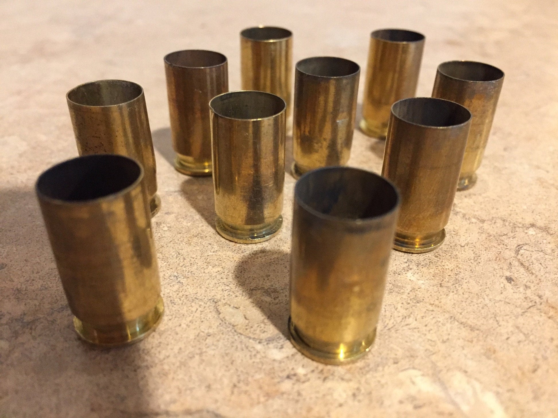 Ten uncleaned brass shell casings arranged horizontally in two rows on a light surface.
