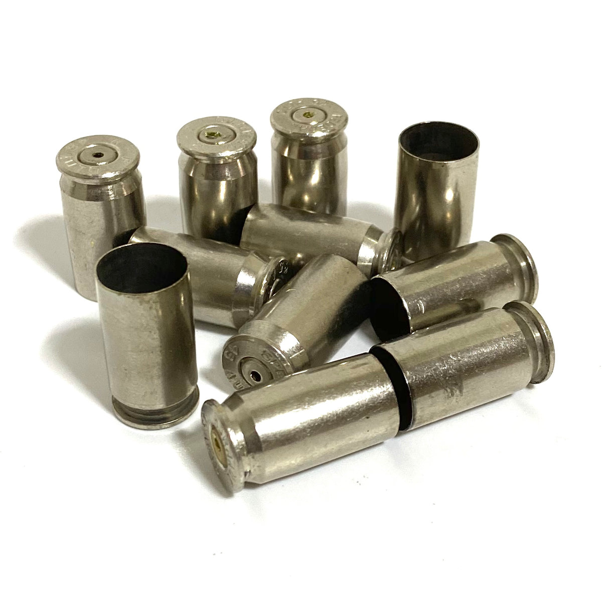 Empty nickel 45 ACP casings with drilled primers, some standing and some lying on a white background