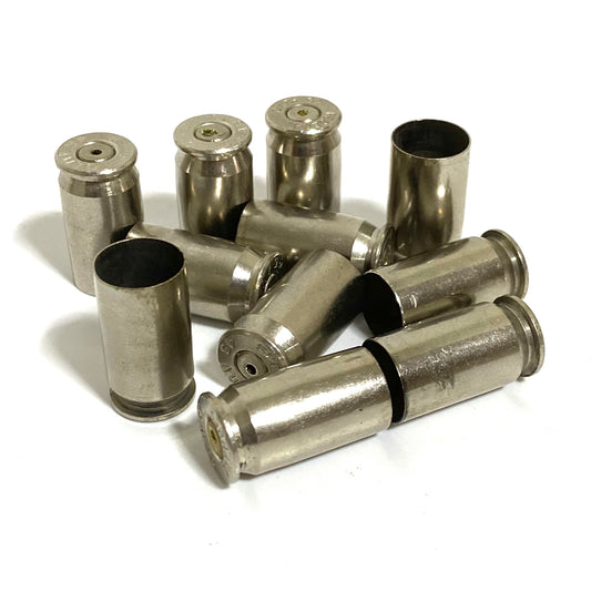 Empty nickel 45 ACP casings with drilled primers, some standing and some lying on a white background