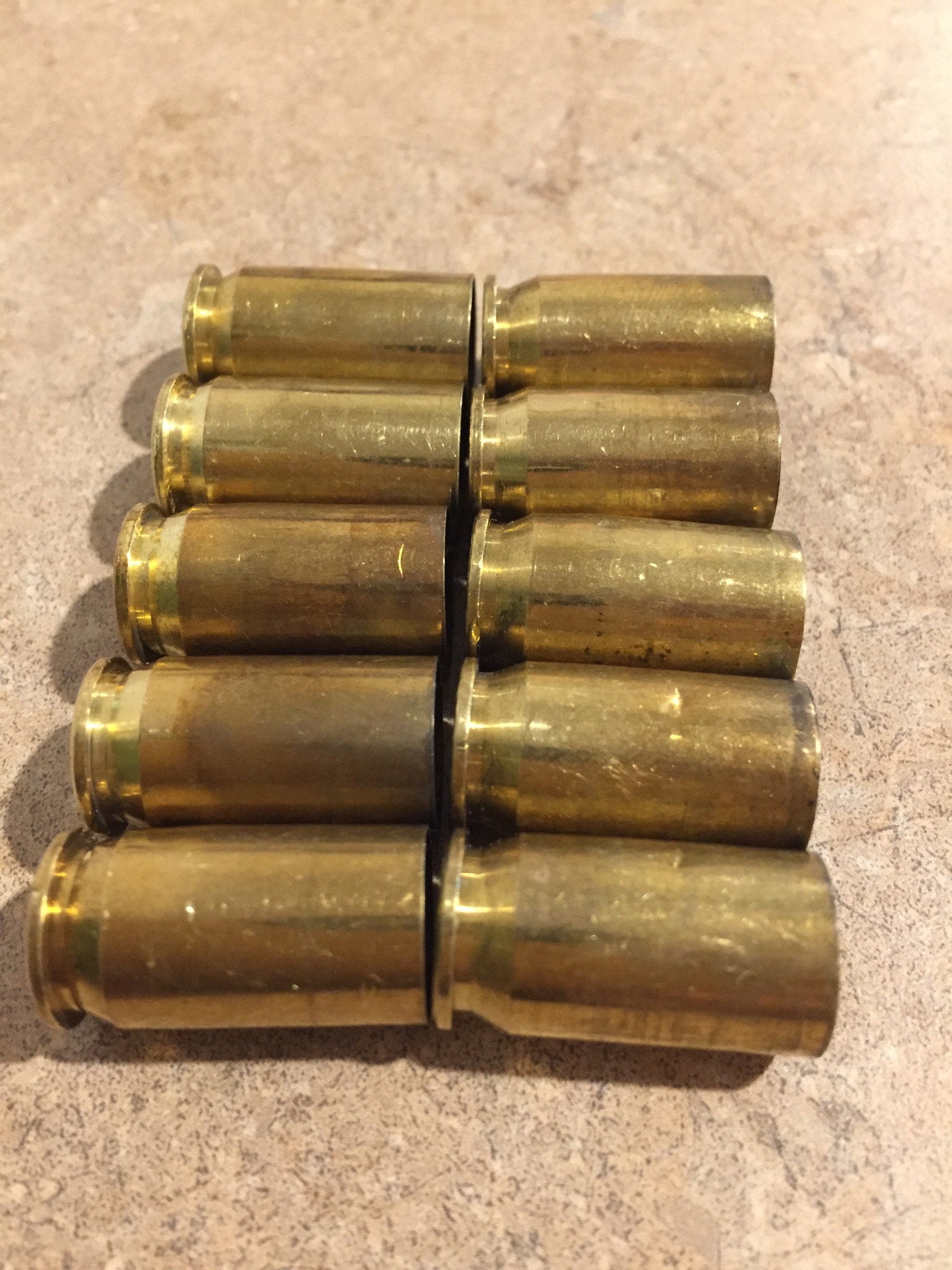 Ten uncleaned brass shell casings arranged in two parallel rows of five on a speckled surface.
