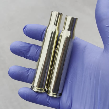 Two highly polished .50 caliber BMG brass casings held in a blue nitrile glove against a white background