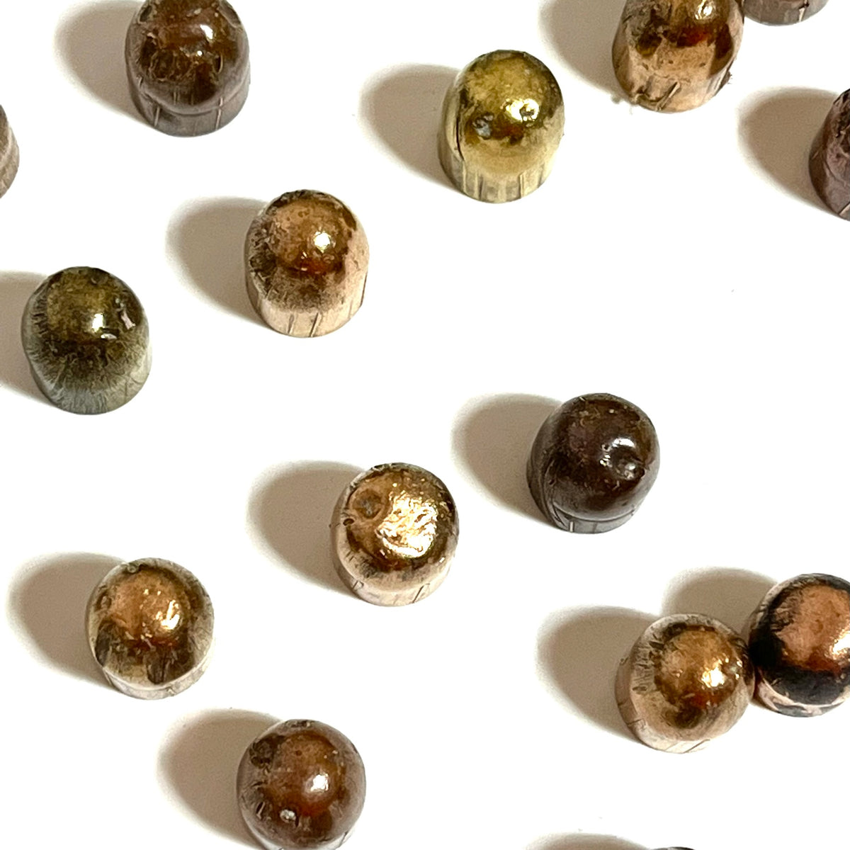 Scattered tarnished copper jacketed 45 ACP fired bullets with flattened tips on a white background