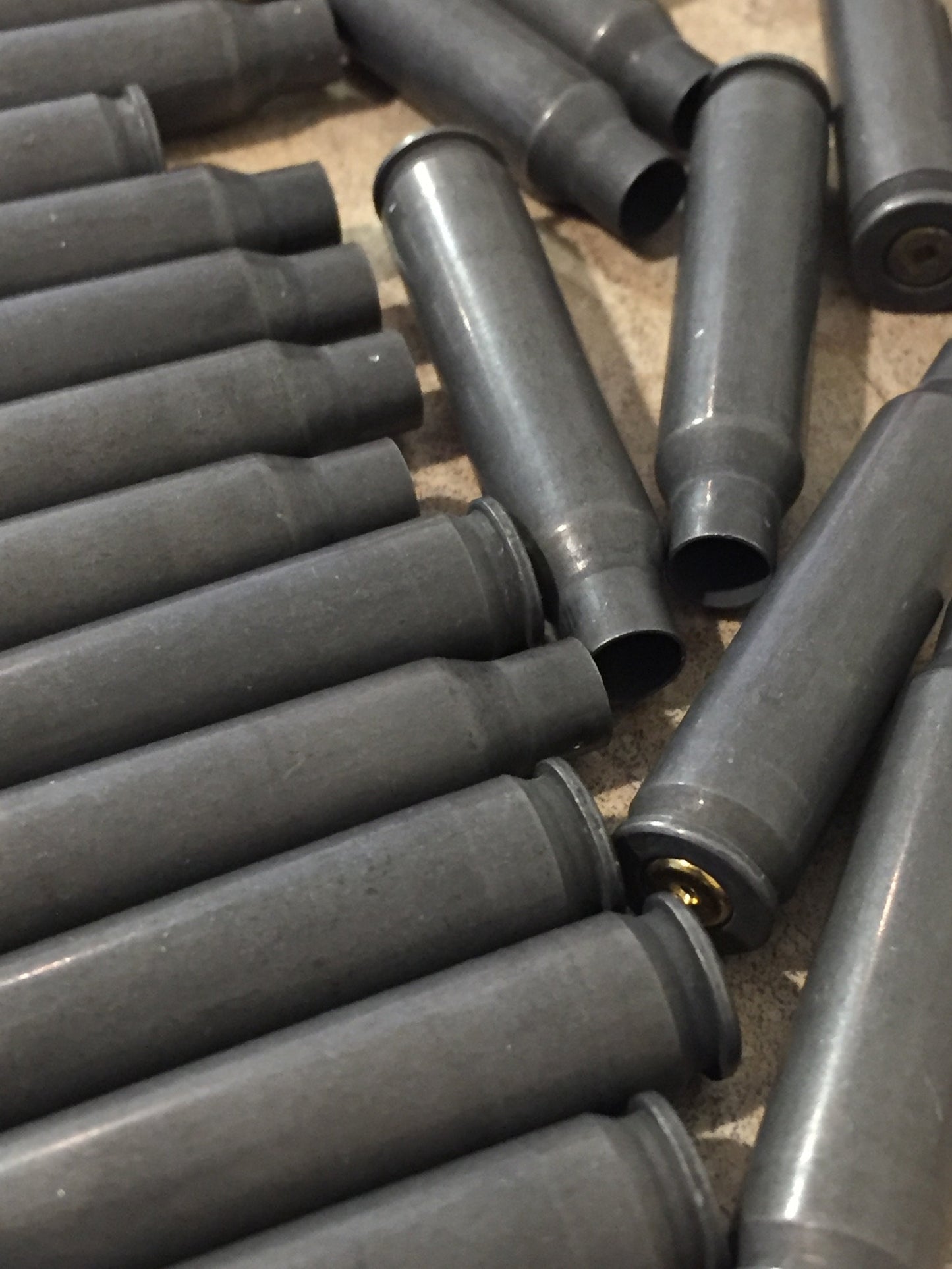 Used gray steel shells lie in overlapping rows on a tan surface, one showing a brass primer.