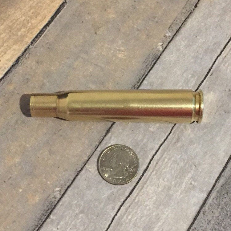 Polished .50 BMG brass casing lying on weathered wood beside a US quarter for size comparison
