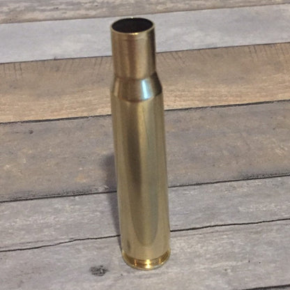 Bright polished .50 BMG brass shell standing upright on gray and tan wood planks
