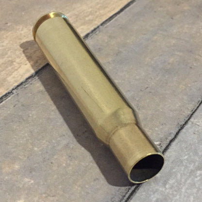 Polished .50 BMG brass casing lying on wood planks with its open case mouth facing the camera