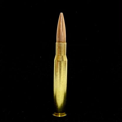 A single shiny 50 BMG weighted paperweight standing upright against a dark black background.
