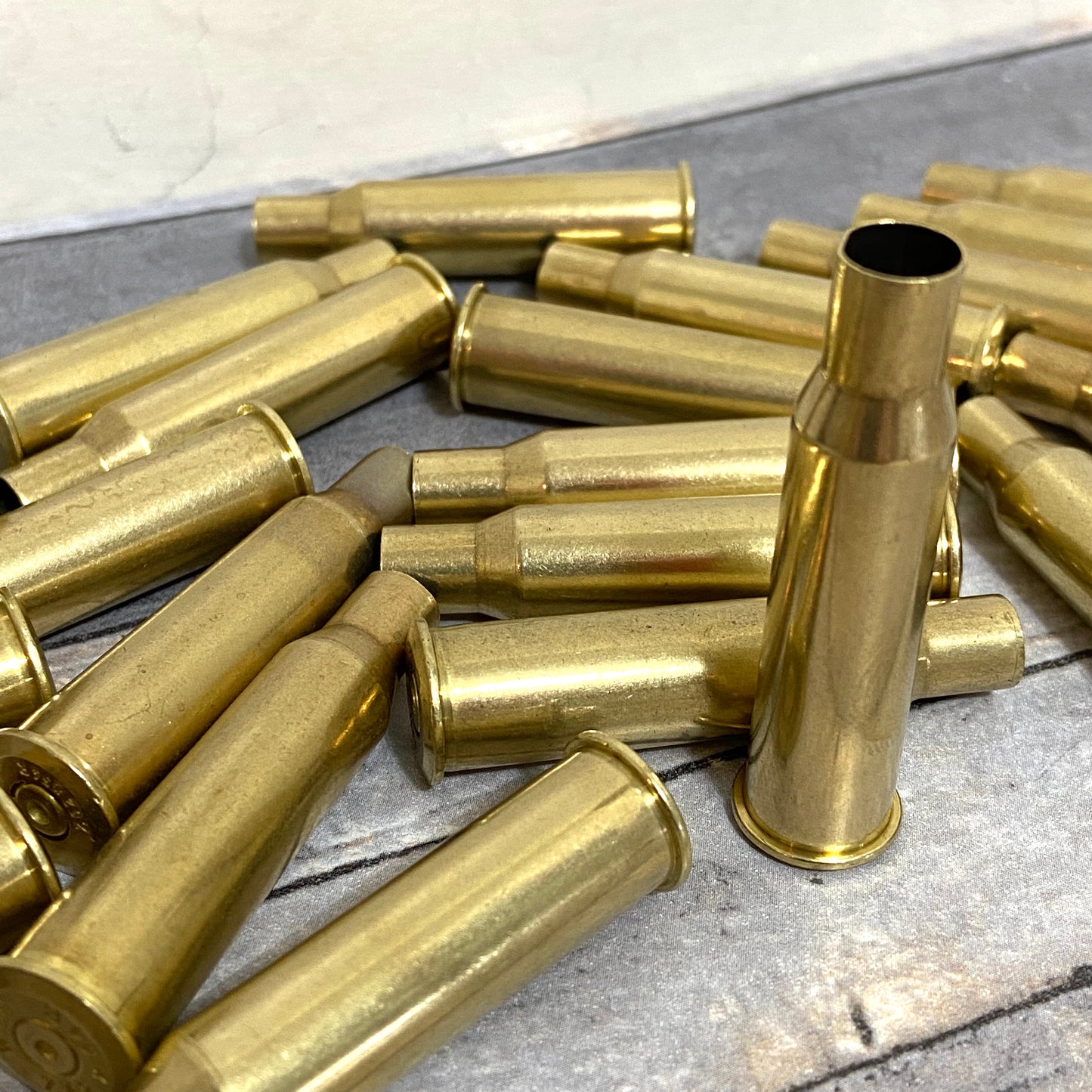 Pile of polished 7.62x54R empty brass rifle casings on weathered wood for steampunk jewelry and upcycled crafting projects.
