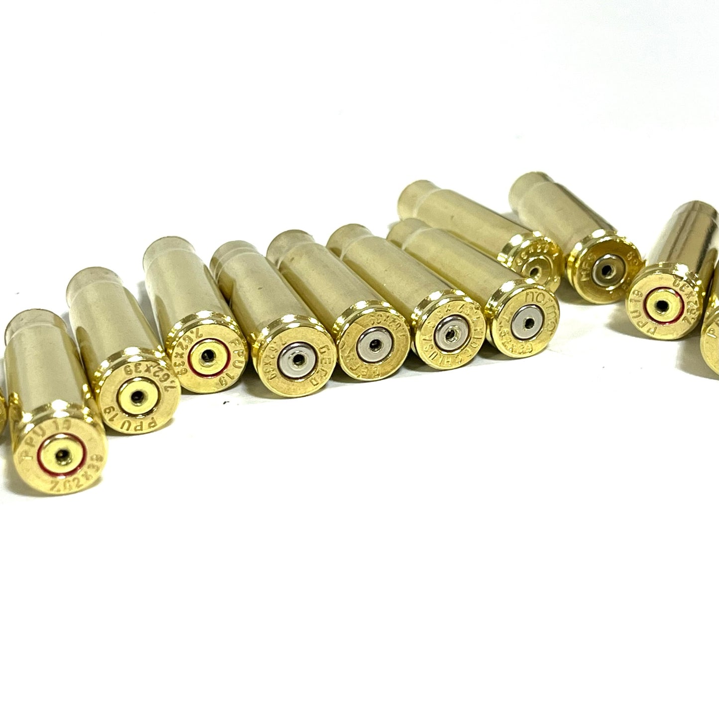 Row of used brass cartridges lying with headstamps facing forward, drilled for jewelry use, on white background.