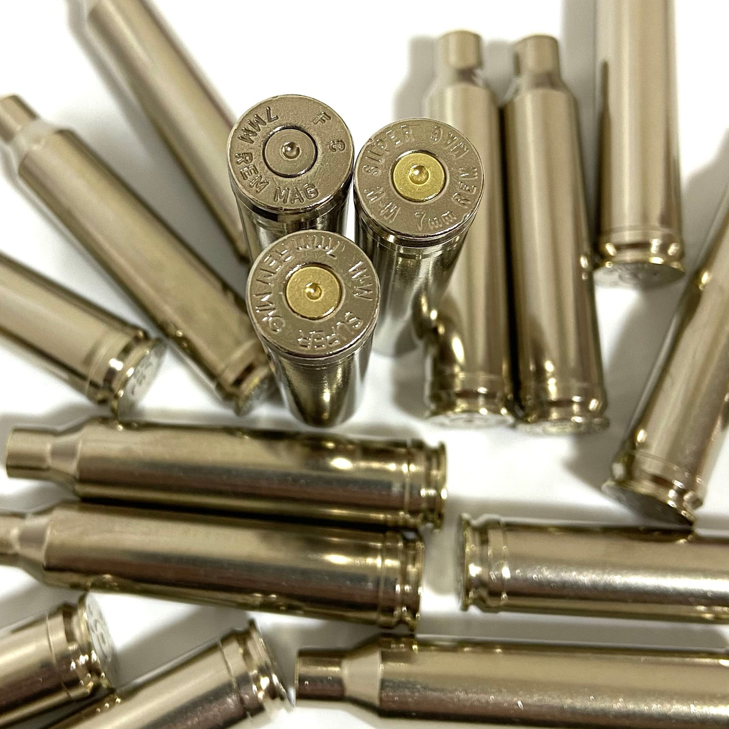 Close-up of nickel-plated 7mm Remington Magnum rifle shell casings showing detailed headstamps and spent primers.
