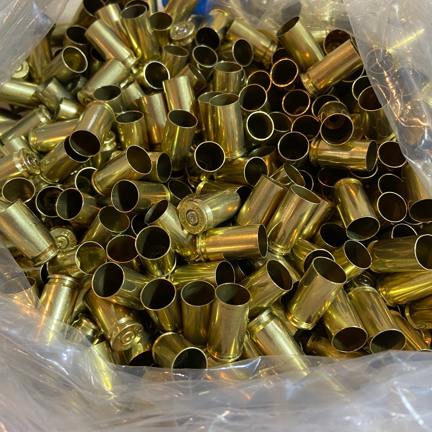 Bulk pile of polished 9mm brass shells in a plastic bag showing open mouths and spent primer dimples.
