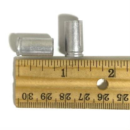 Two silver aluminum 9mm casings measured on a wooden ruler for craft sizing reference.